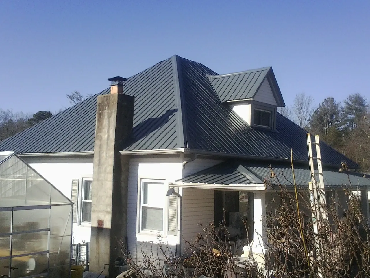 Dark blue standing seam metal roof on a white farmhouse with dormer — Slate & Tile Roof Repair by Roofing Brothers in Leasburg