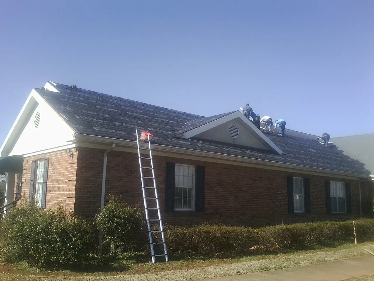 Crew tearing shingles off a brick ranch roof with a ladder set — Metal Roof Repair work by our crew in Leasburg