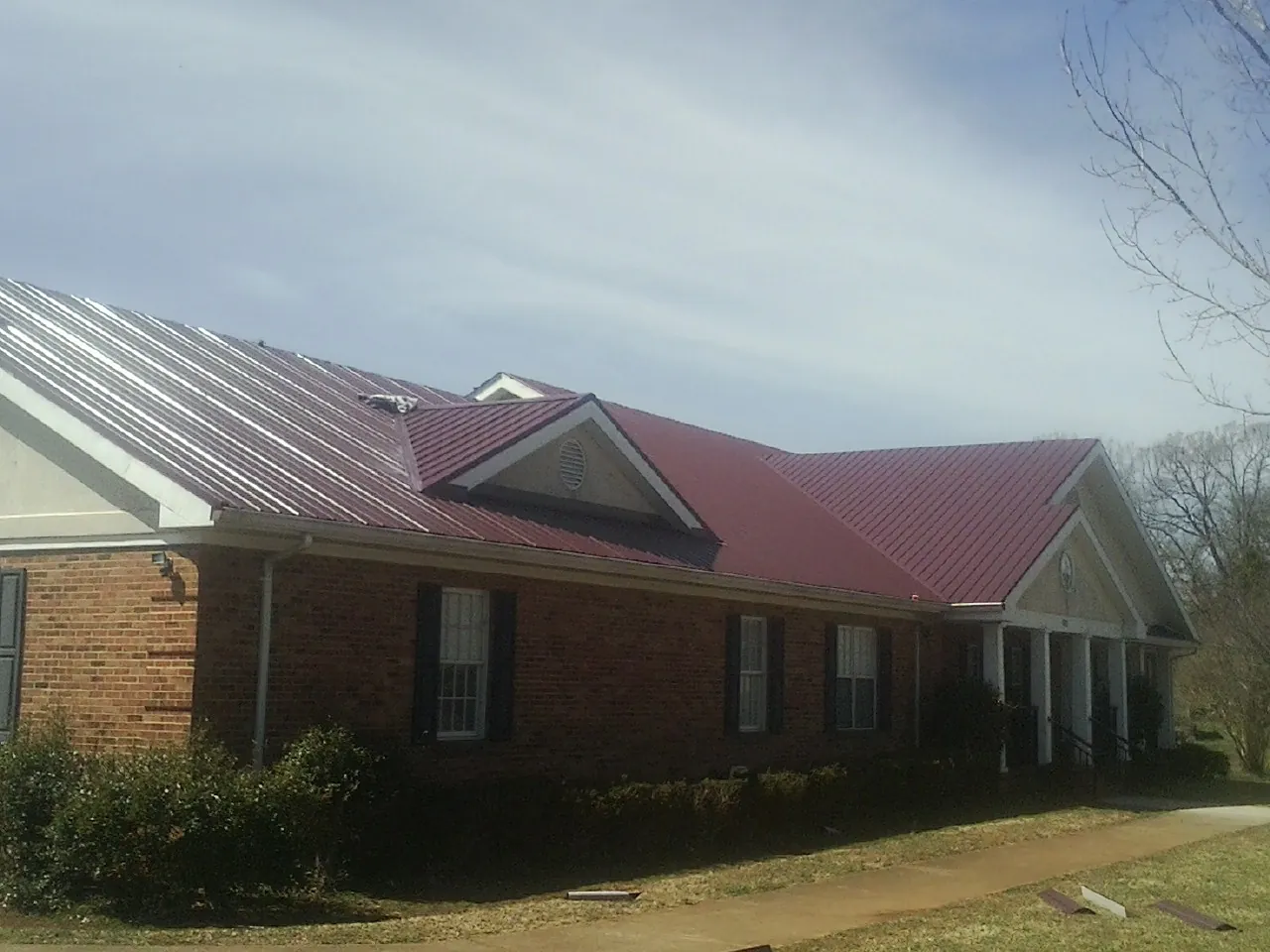 Red metal roof with gabled entries on a long brick building, from a Hail Damage Roof Repair job in Leasburg